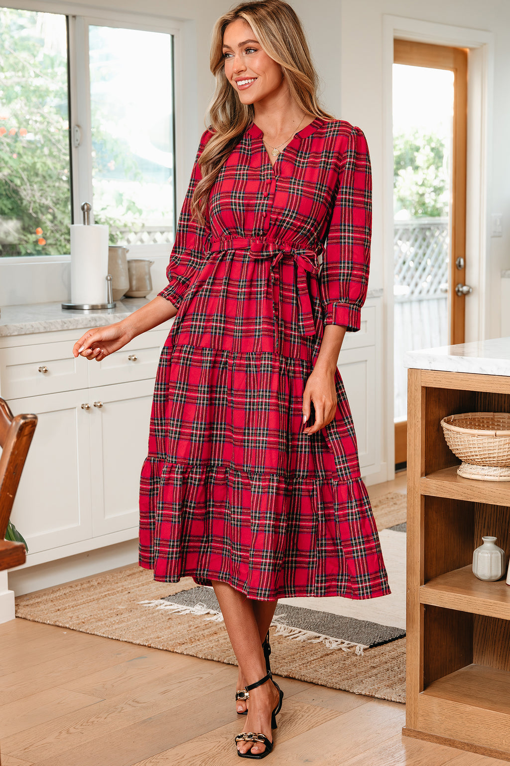 Woman in kitchen wearing red plaid midi dress with waist tie and black heels