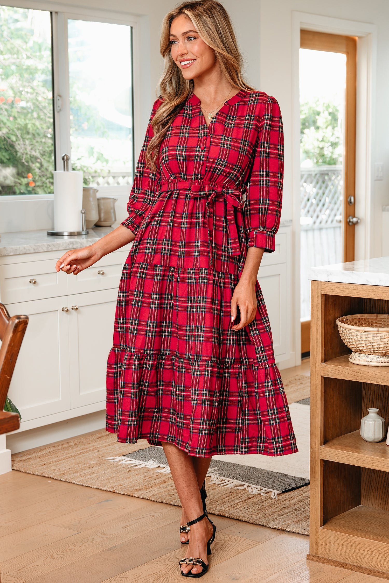 Woman in kitchen wearing red plaid midi dress with waist tie and black heels