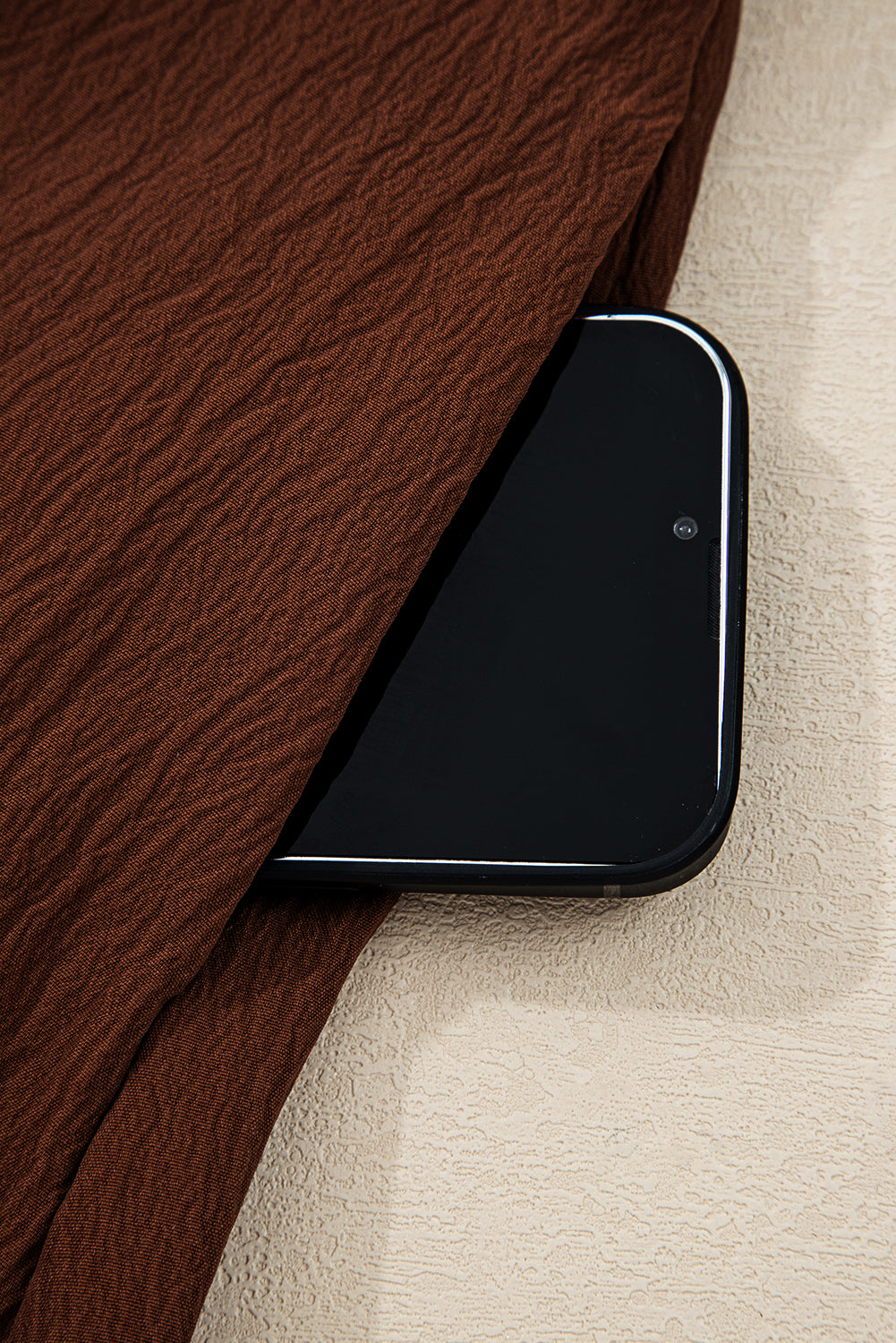 Black smartphone in brown textured fabric pocket on light textured surface