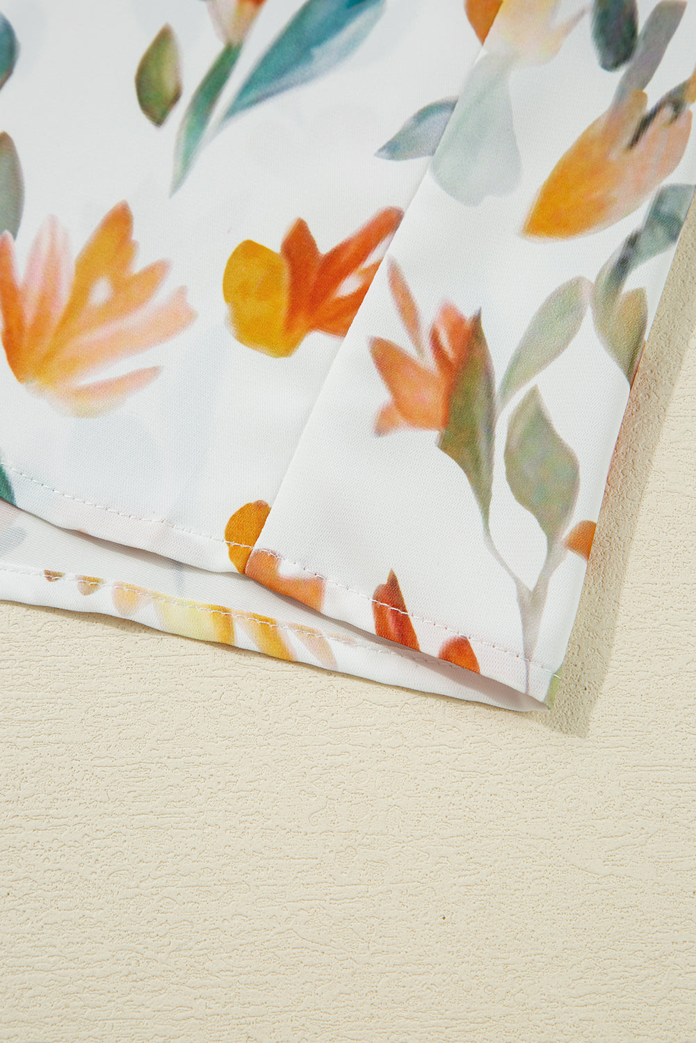Close-up of white fabric with orange and green floral print and cleanly stitched hem.
