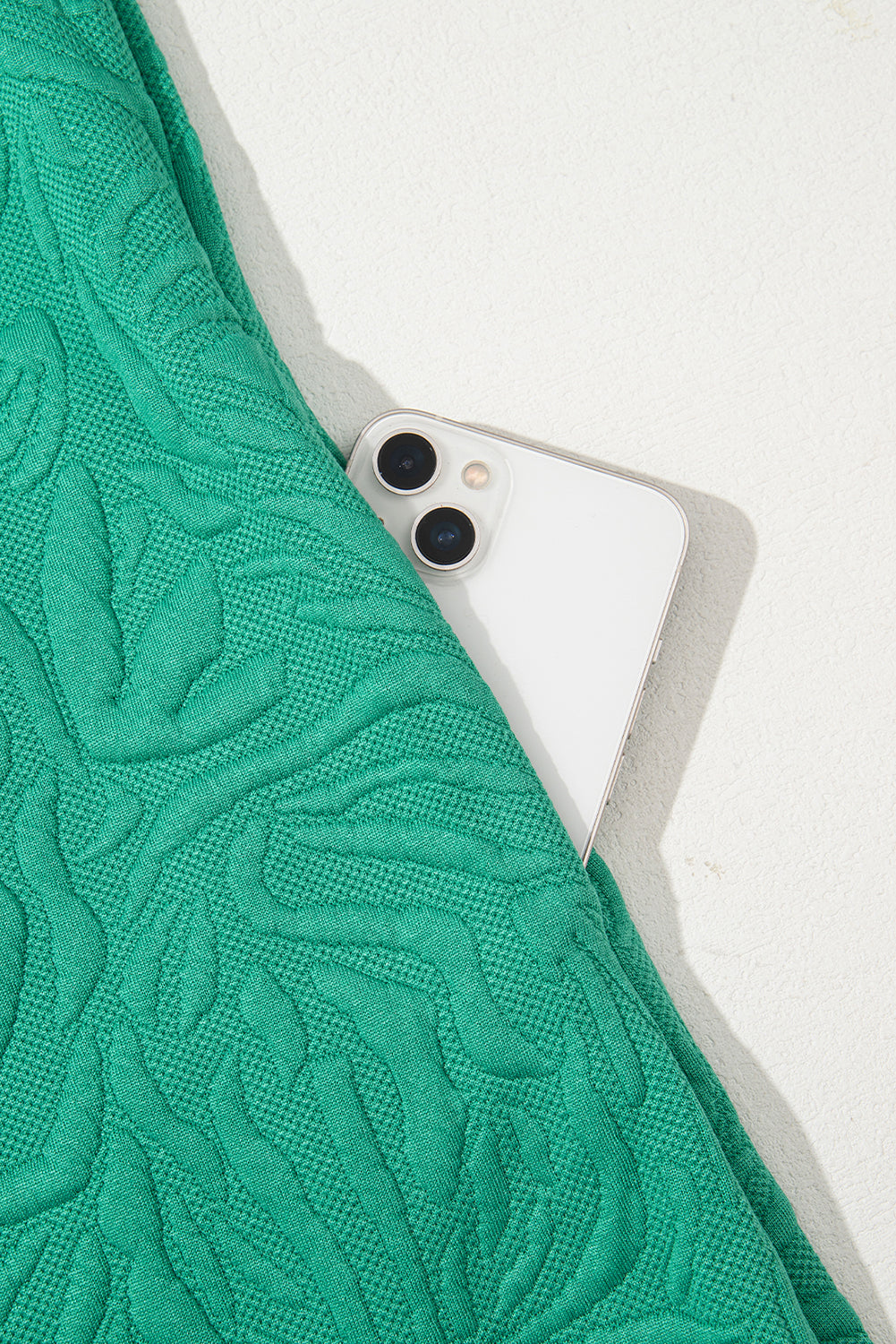 White smartphone in pocket of textured green fabric garment on a light surface