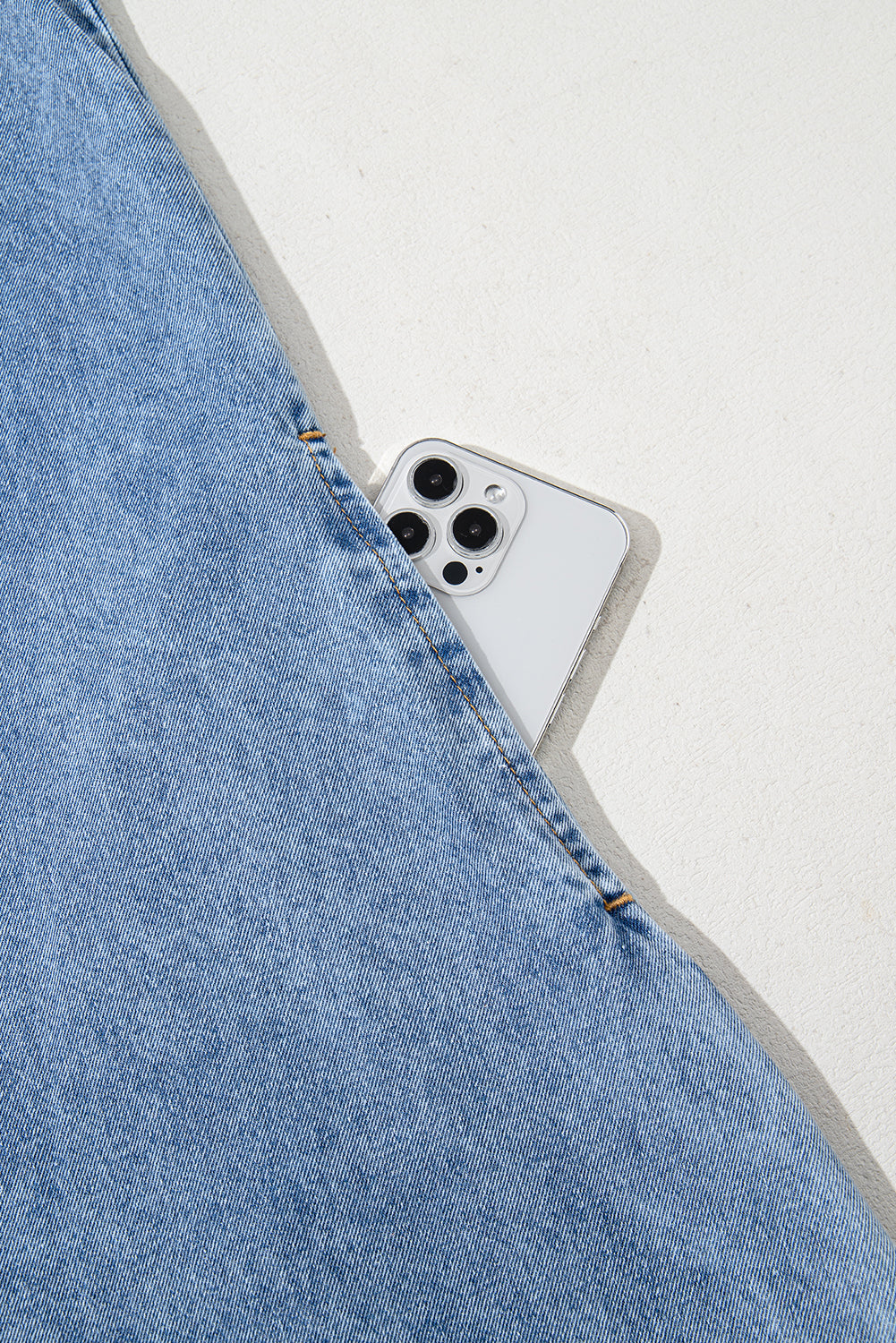 Blue denim pocket with smartphone partially visible inside, minimalist background