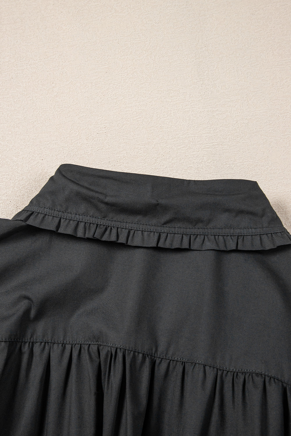 Black ruffled collar shirt detail with gathered fabric, close-up on textured background