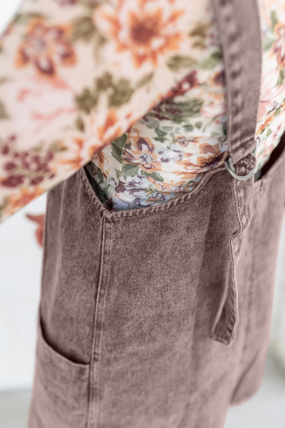 Close-up of a person wearing a pink corduroy overall dress and a floral long-sleeve top