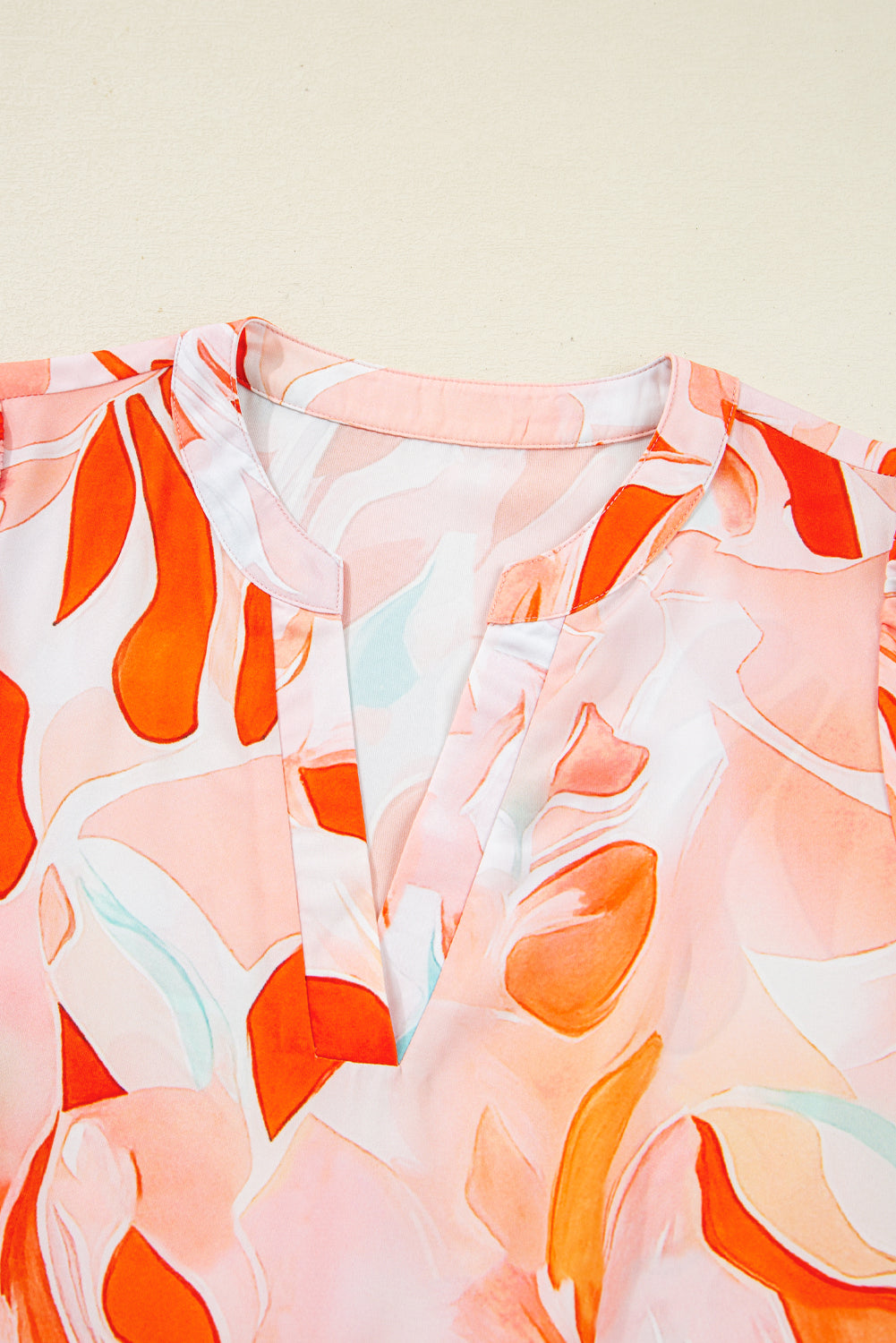 Close-up of a women's blouse with orange and pink abstract floral pattern and split neckline