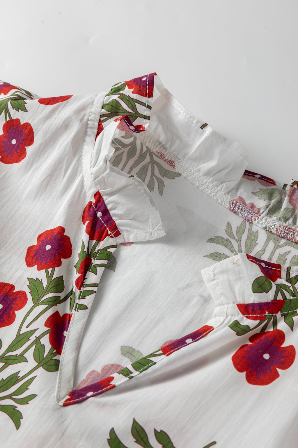 White blouse with red floral print and ruffled neckline close-up