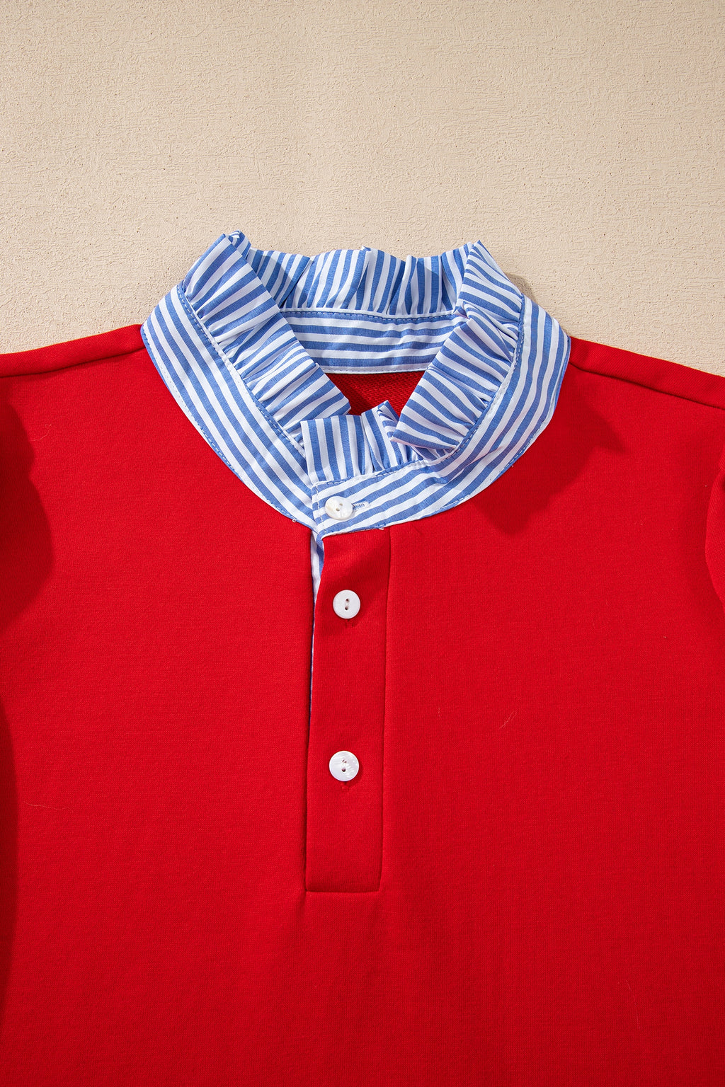 Red blouse with white buttons and blue white striped ruffle collar on beige background
