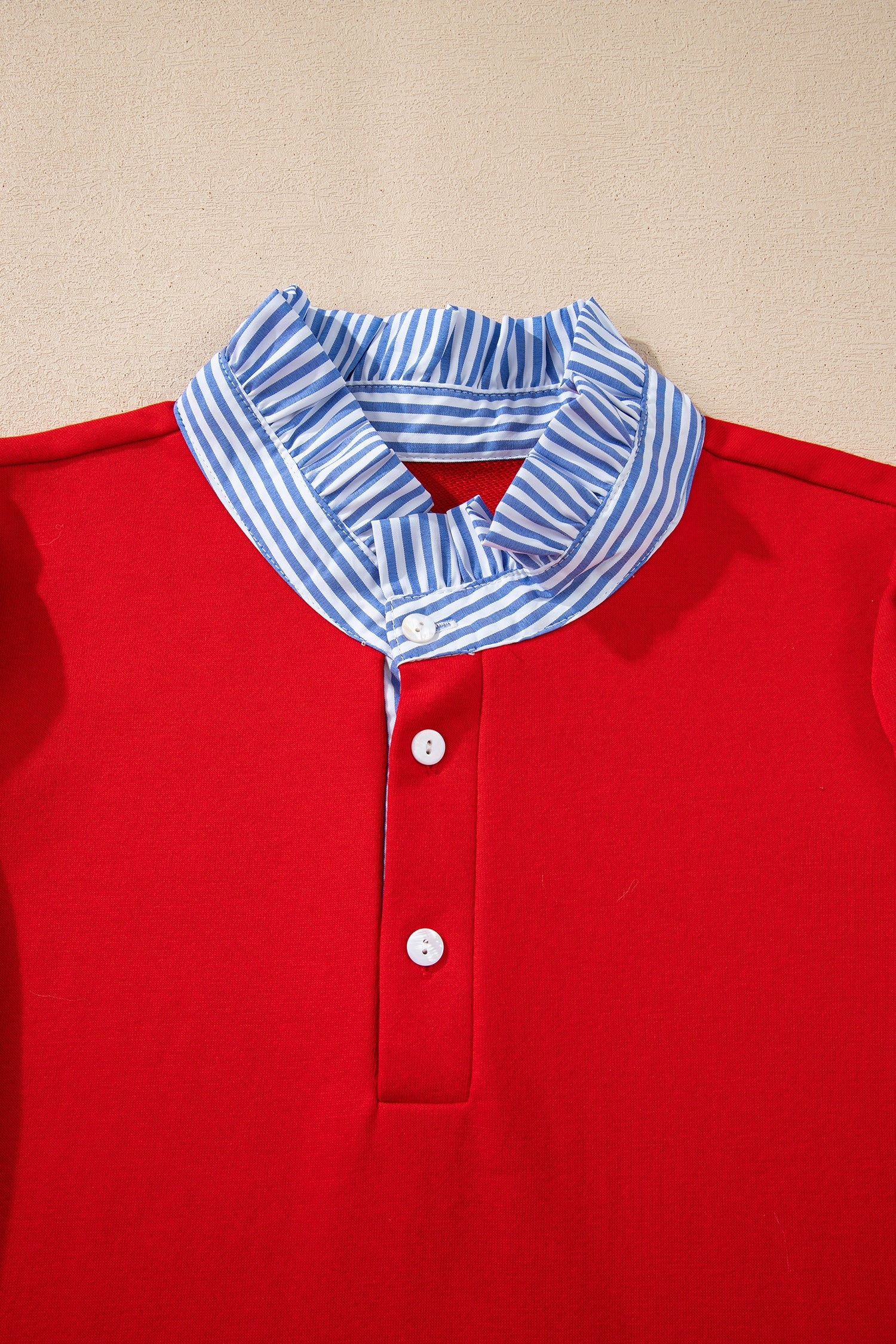Red blouse with white buttons and blue white striped ruffle collar on beige background