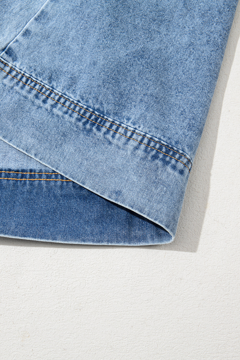 Close-up of light blue denim pant hem with double stitching detail on white surface