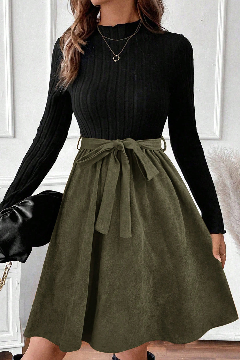 Woman in a long sleeve black top and olive green A-line skirt with waist tie, stylish outfit