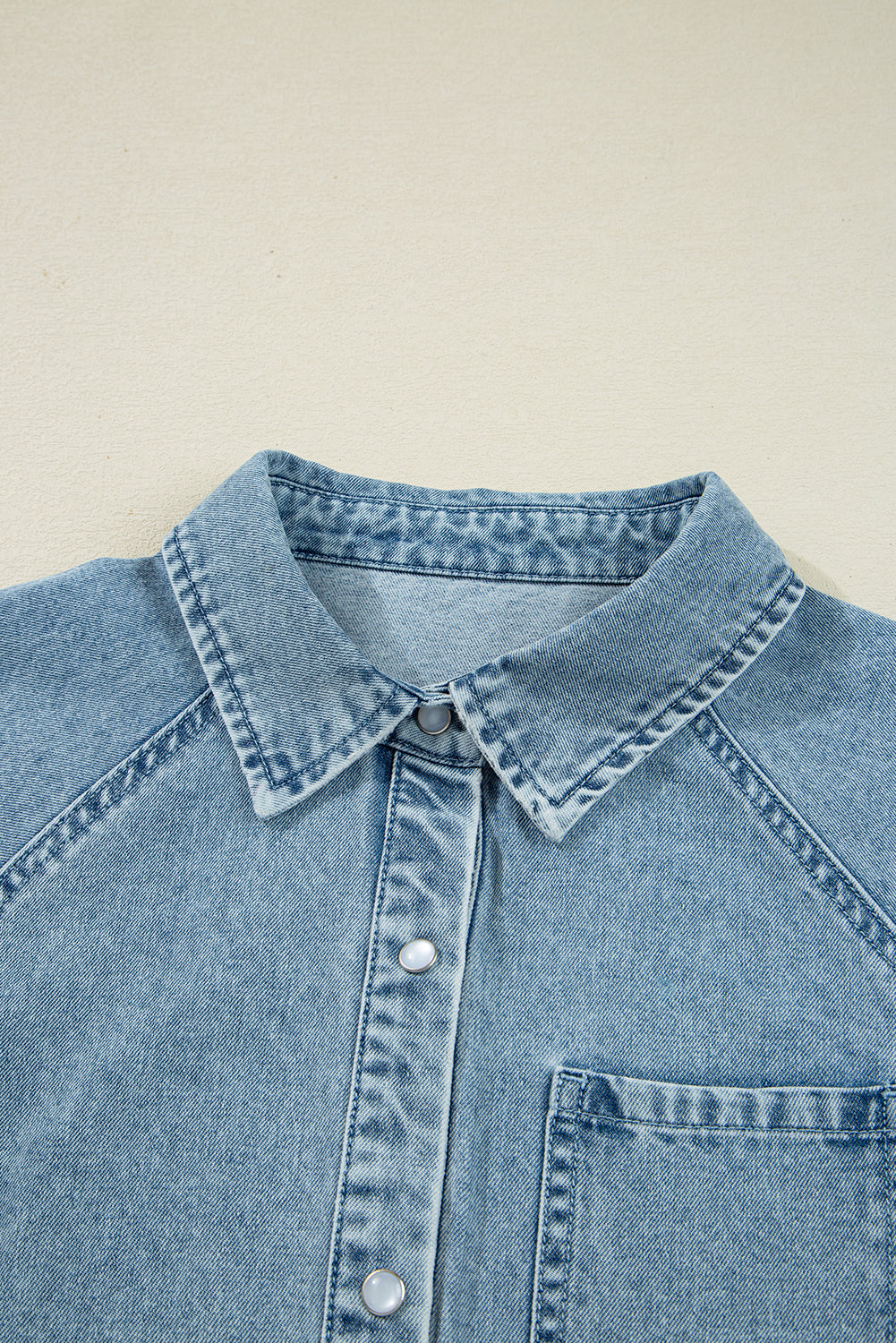 Light blue denim shirt with snap buttons and chest pocket on neutral background