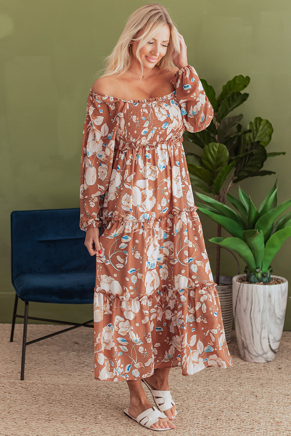 Woman wearing a brown floral off-shoulder maxi dress with long sleeves, standing indoors.