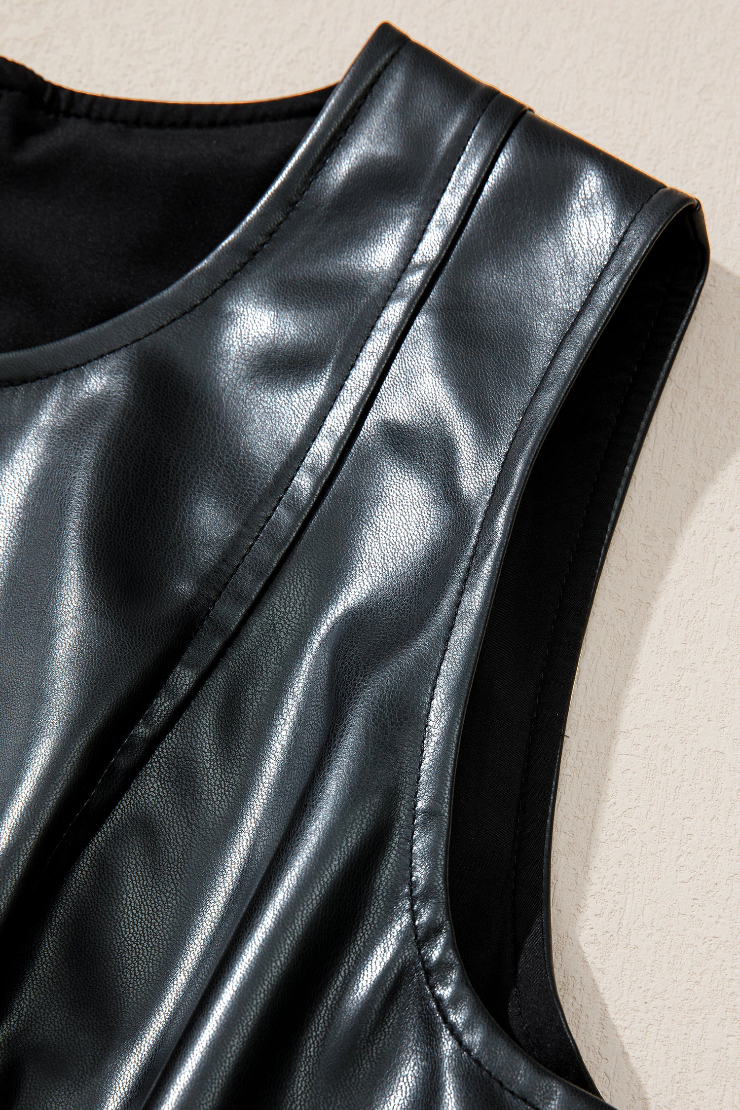 Close-up of black faux leather sleeveless top with round neckline and textured shine.