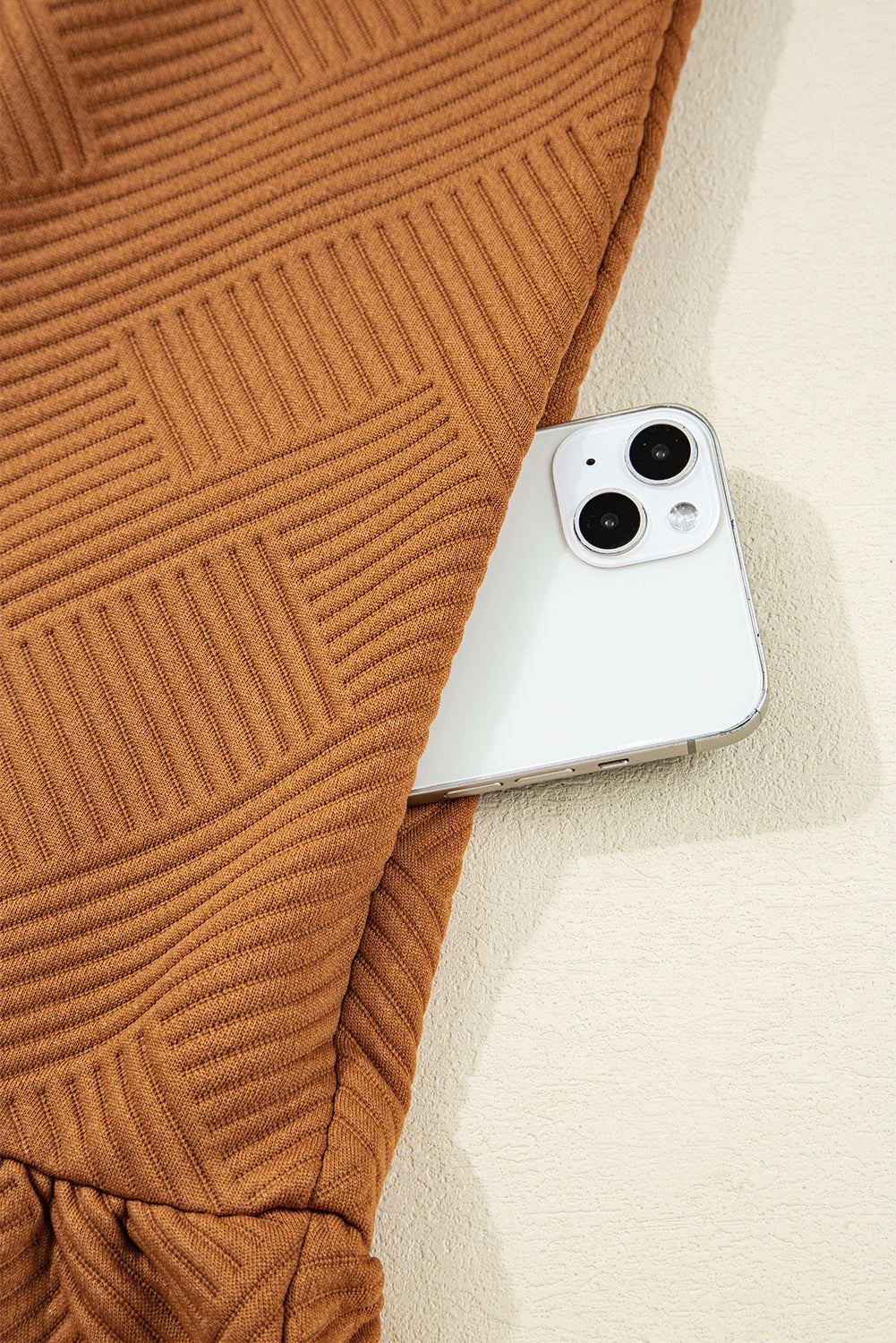 Brown textured knit garment with a white smartphone partially tucked in a pocket