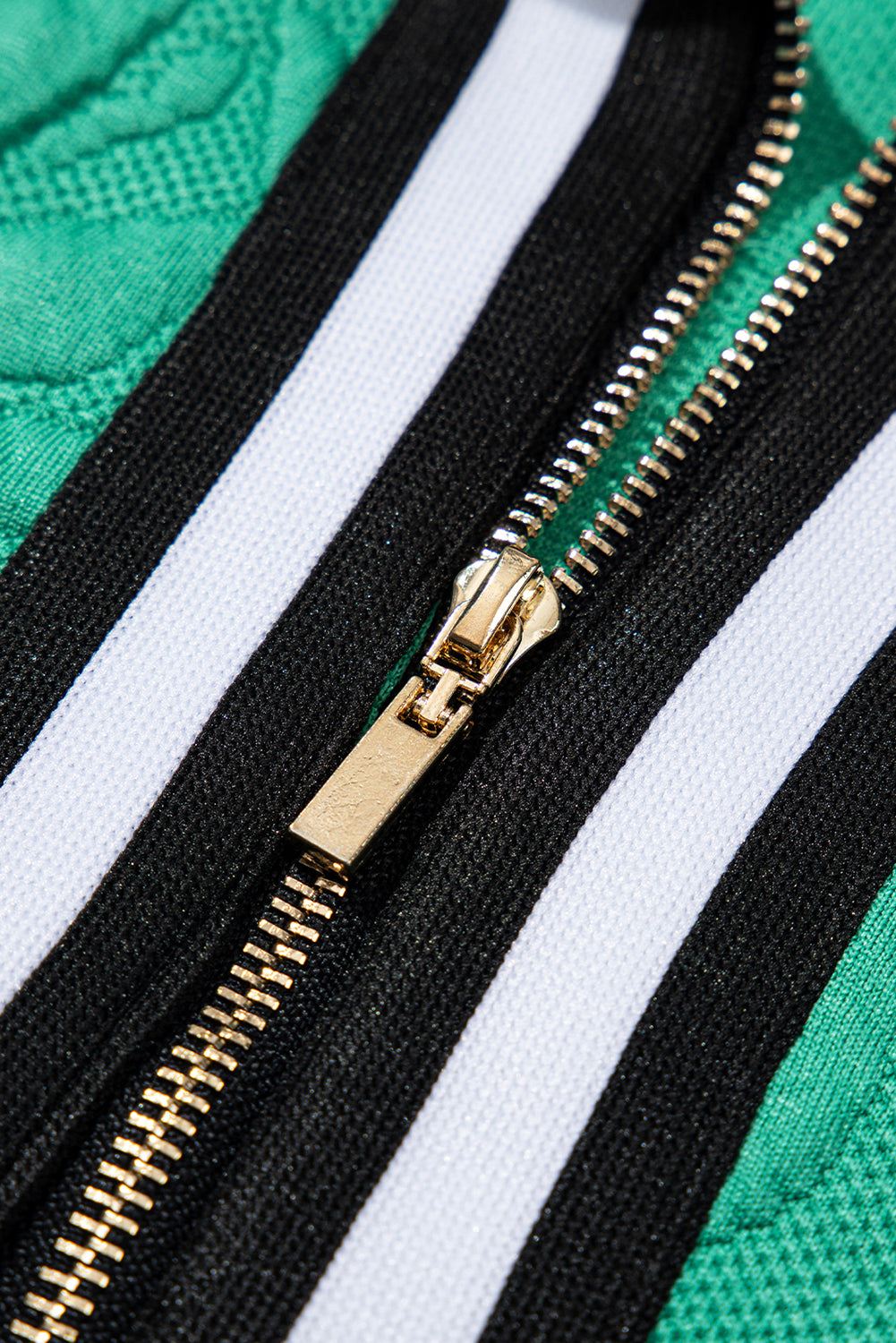 Gold zipper on green fabric with black and white stripes, clothing close-up