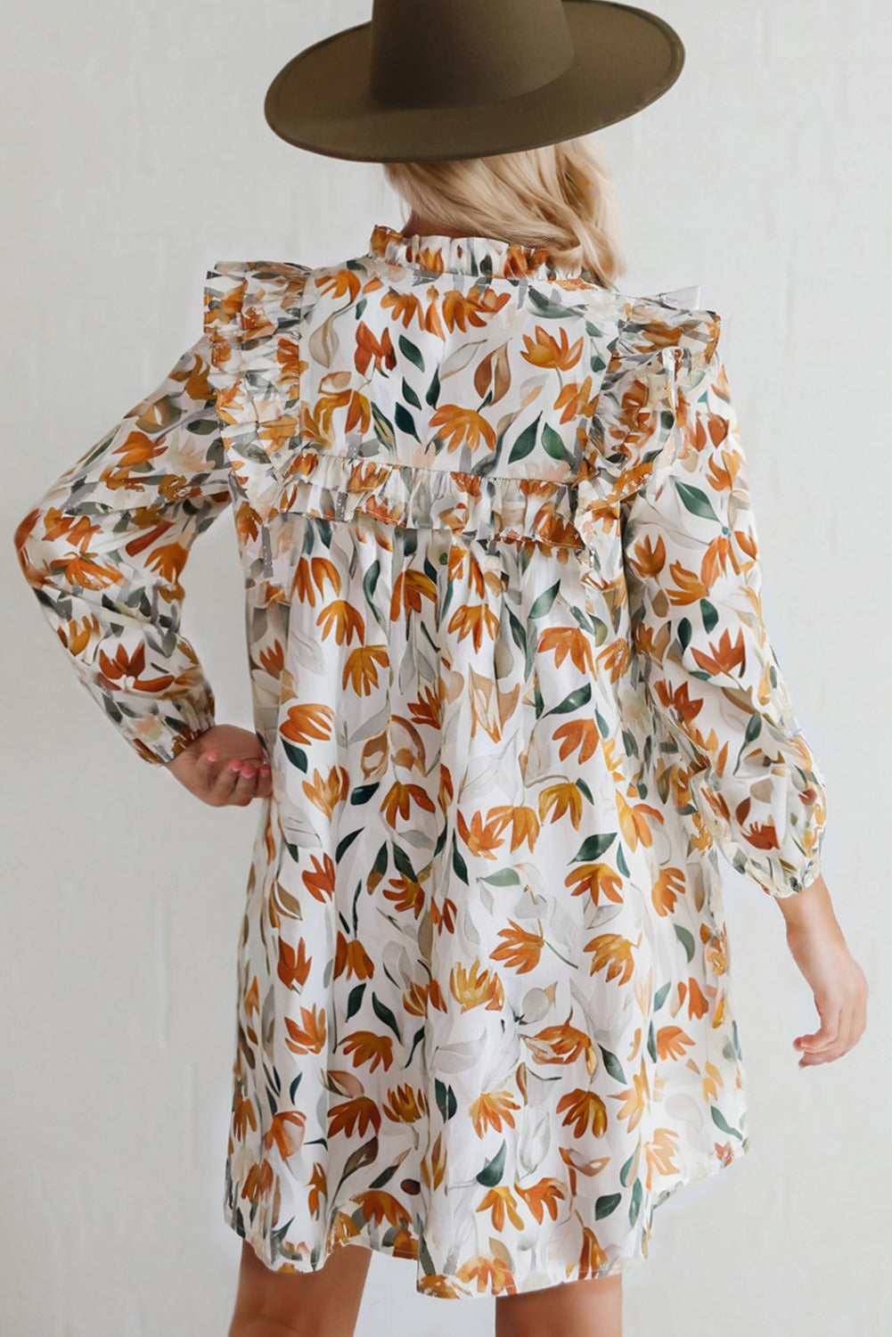 Woman in a wide-brim hat wearing a long-sleeve floral ruffle dress with orange and green leaf print