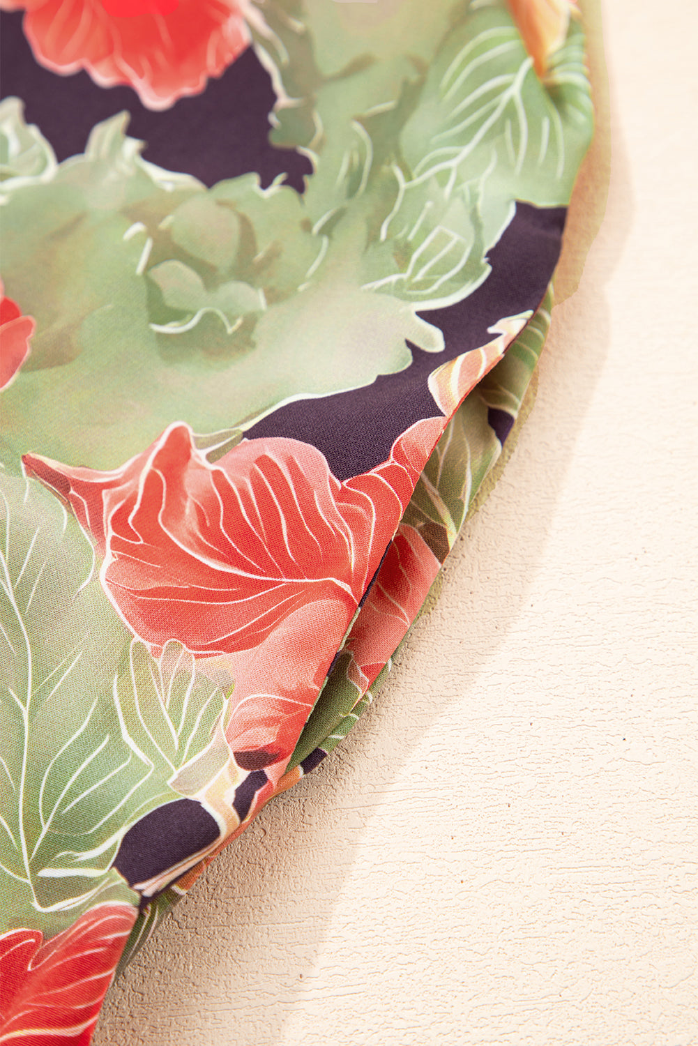 Close-up of fabric with green leaves and red floral print, textured background