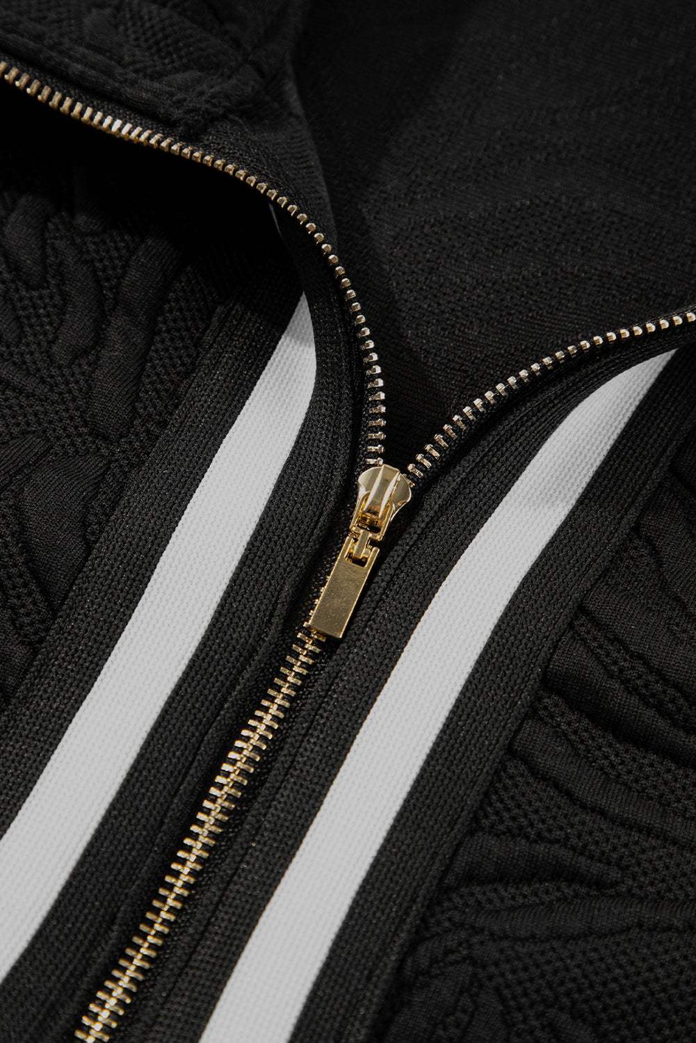 Close-up of a black textured jacket with gold zipper and white stripes