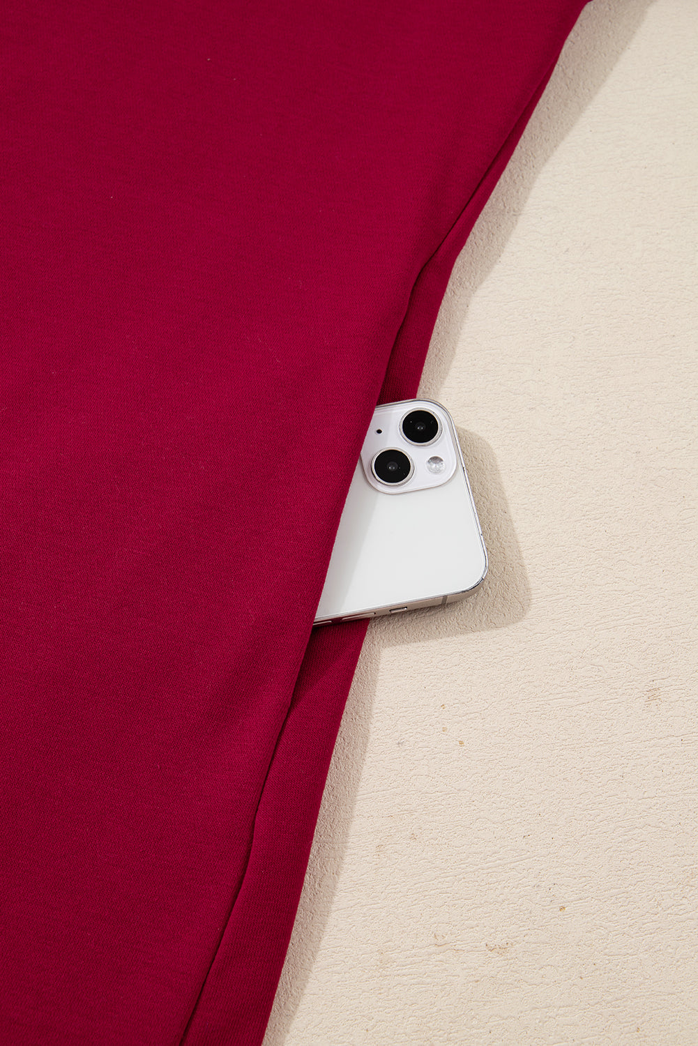 Close-up of maroon fabric pants with a phone in the pocket on a beige background